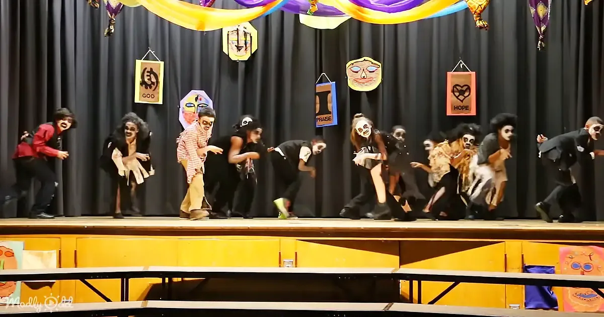 Actors in zombie costumes perform on stage with "GOD," "HOPE," and "PRAISE" signs in the background.