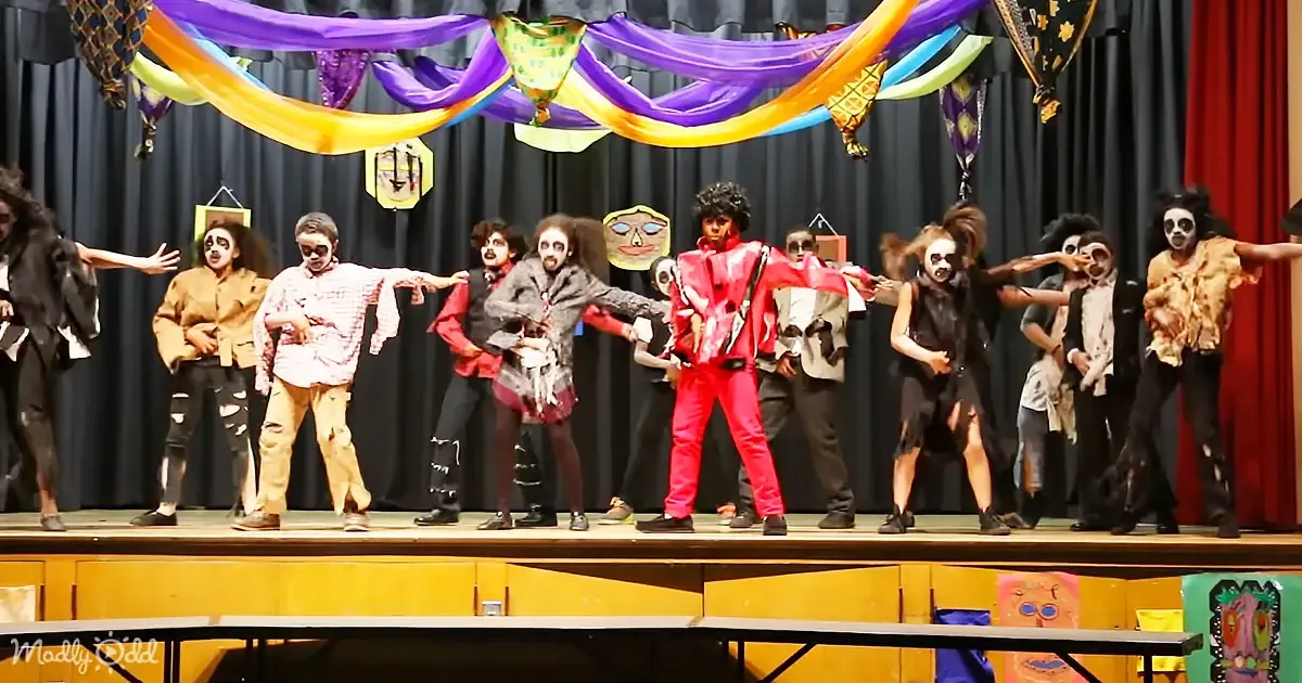 A performer in a red outfit dances center stage, surrounded by a group in zombie costumes.
