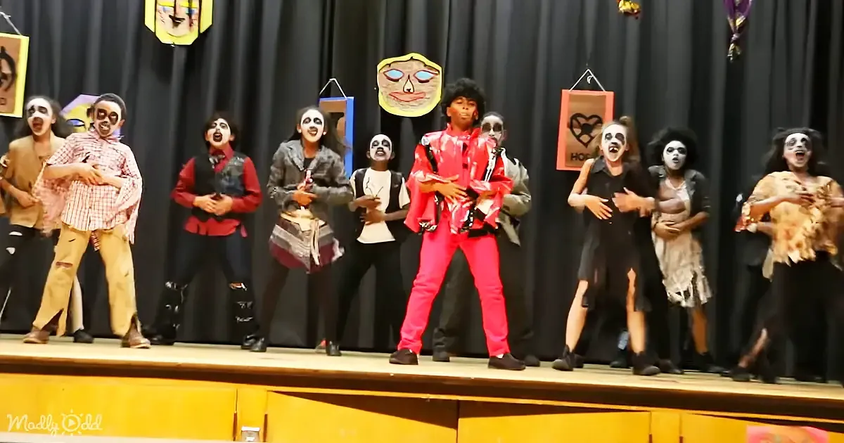 A person in a red outfit dances on stage, surrounded by others in zombie costumes.