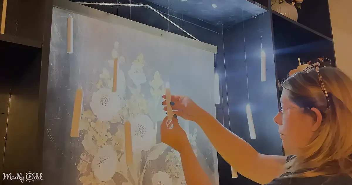 A person is arranging candles on a floral backdrop in a dimly lit room.