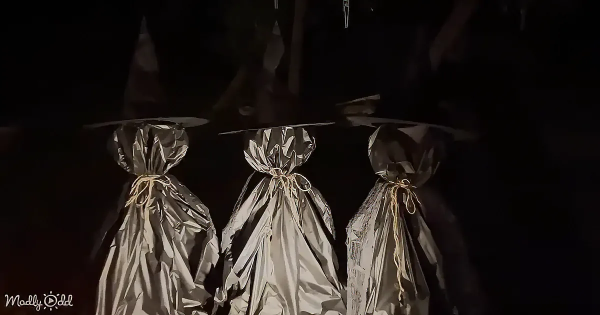 Three figures wrapped in silver foil with pointed hats stand in a dark, eerie setting.