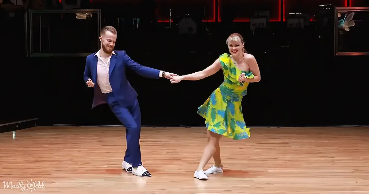 A couple in vibrant outfits dances gracefully on a wooden floor, showcasing their skill and chemistry.