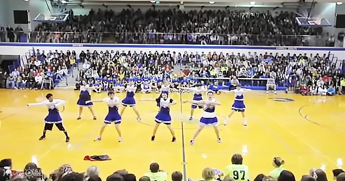 Cheerleaders in blue and white uniforms perform a routine on a basketball court with a large audience watching.