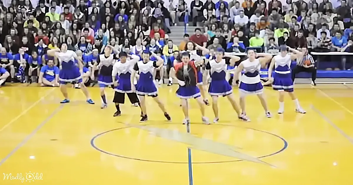 Cheerleaders in blue and white uniforms perform on a basketball court with a crowd watching.