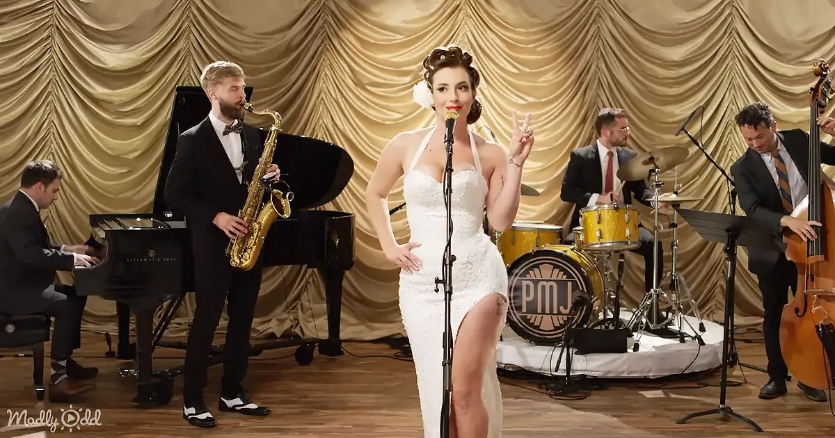 A woman in a white dress sings on stage with a band playing jazz music.