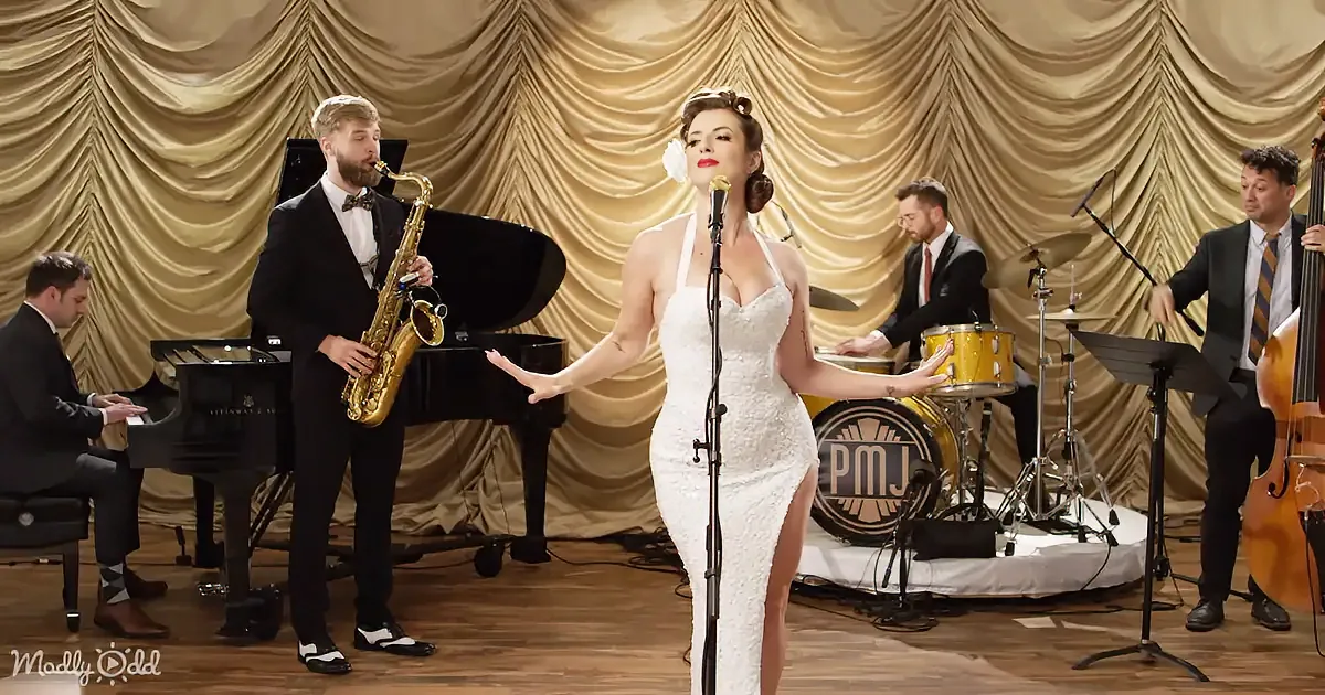A woman in a white dress sings on stage with a band playing jazz music.