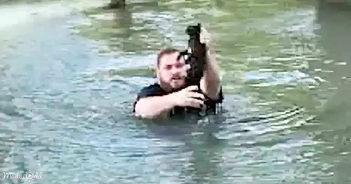 A man in water holds a small dog, both partially submerged, with the dog's head above water.