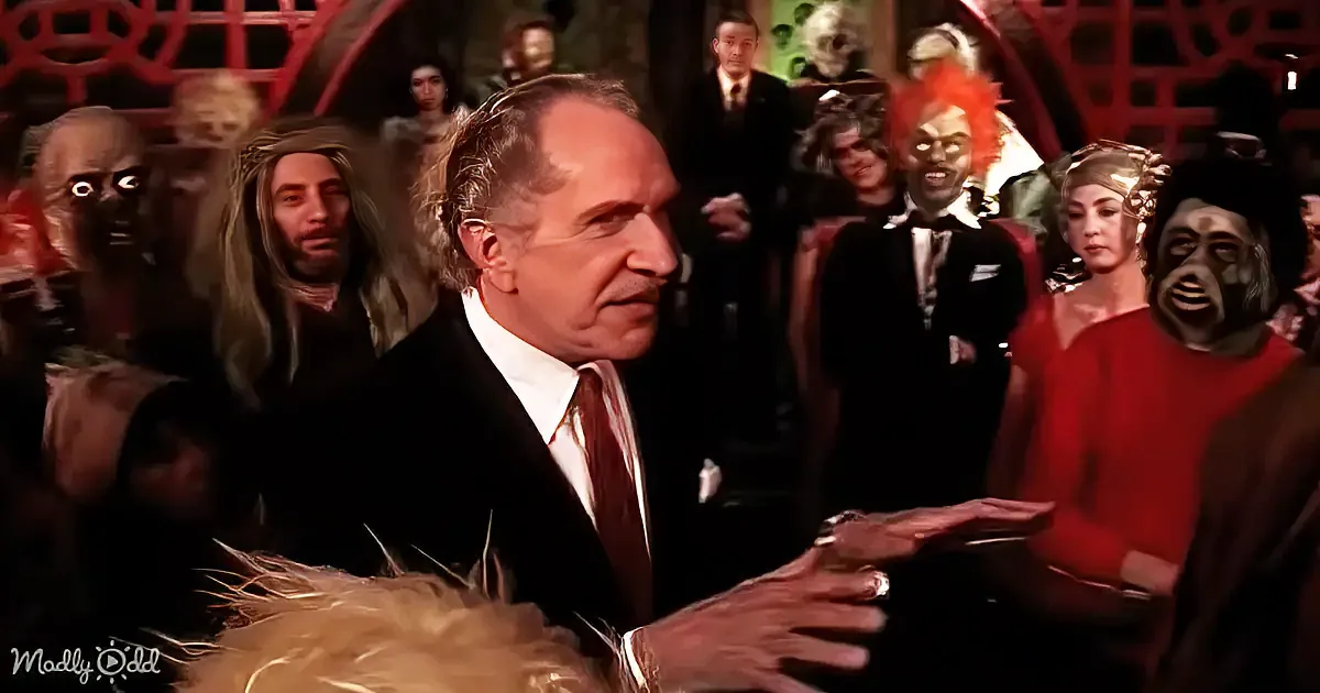A man in a suit extends his hand, surrounded by a crowd of people in various costumes and masks.