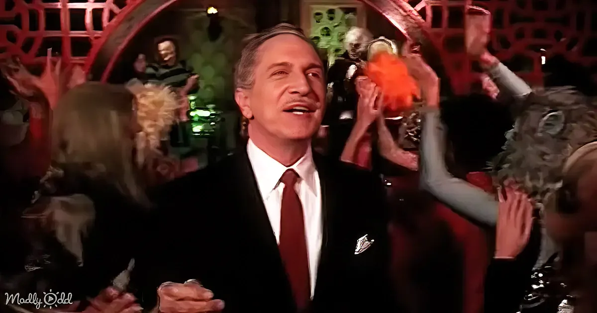 A man in a suit and tie smiles amidst a crowd of people raising their hands.
