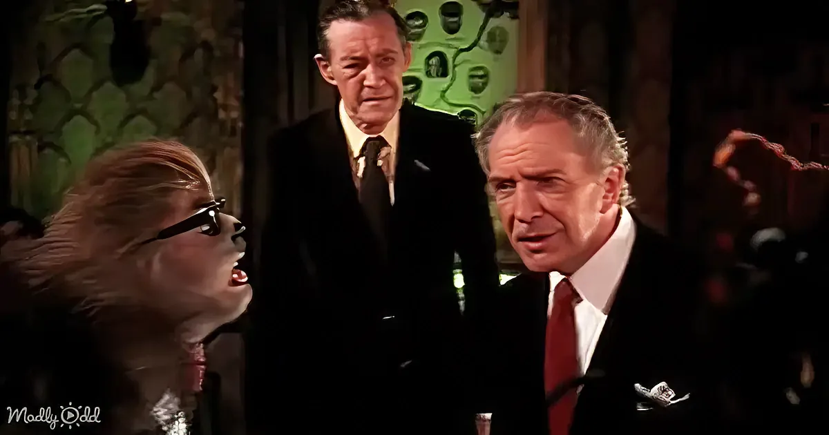 A woman in a black outfit and sunglasses is yelling, while two men in suits look on in a dimly lit room.