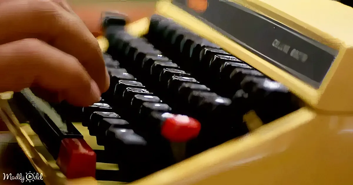 A close-up of a hand typing on a vintage yellow and black typewriter.