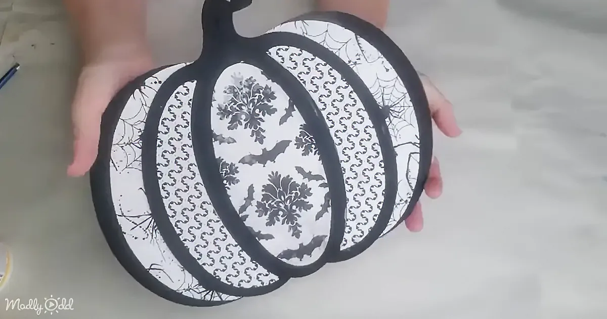 A person holds a black pumpkin-shaped object with a white pattern featuring bats and spider webs.