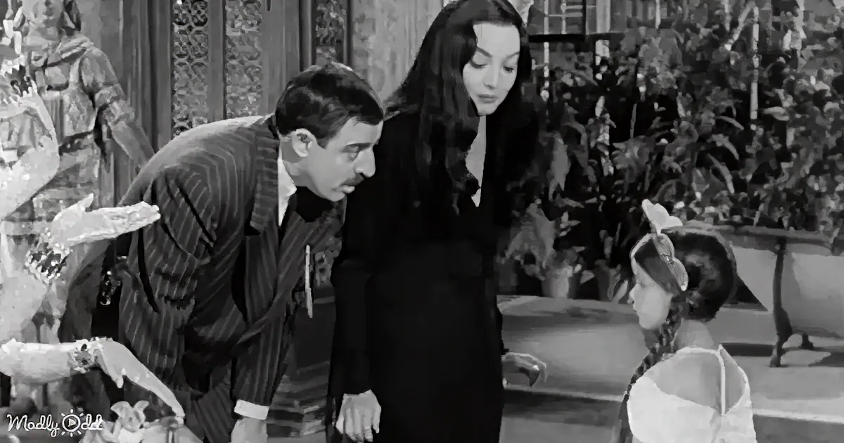A man in a striped suit leans forward, looking at a young girl in a white dress, while a woman in a black dress stands...