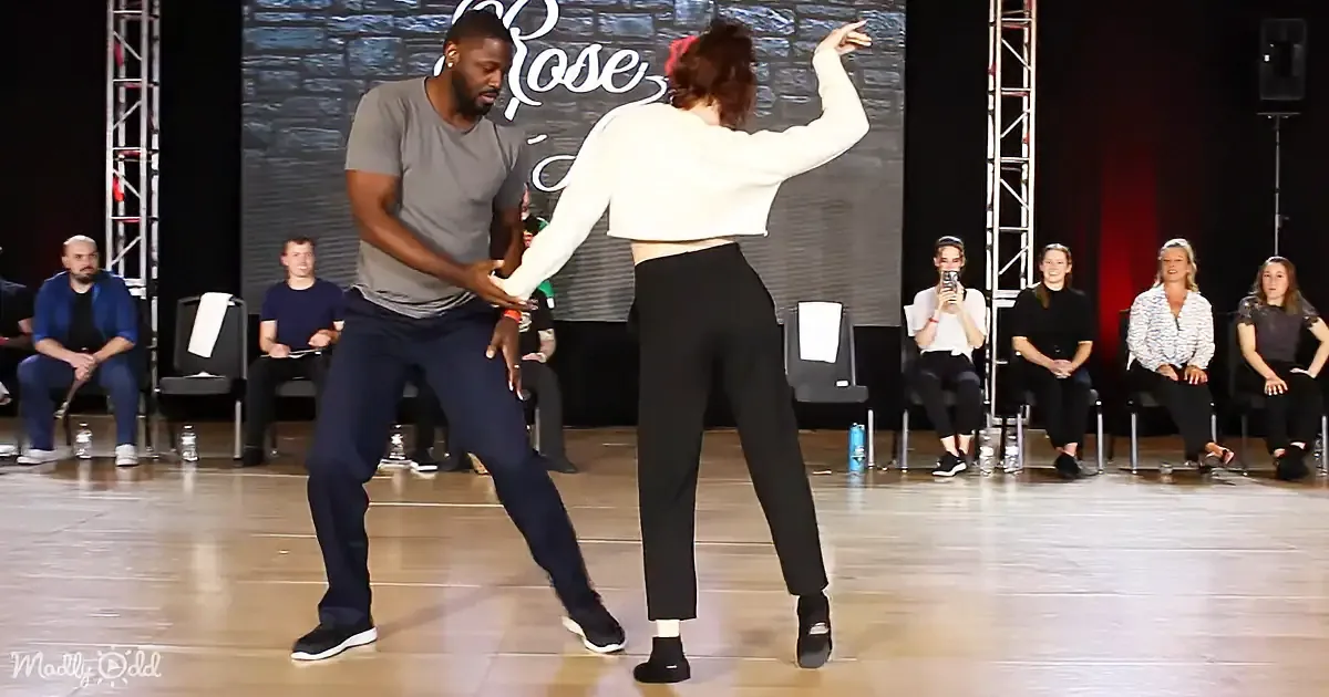A man and woman dance together on stage, surrounded by an audience watching.