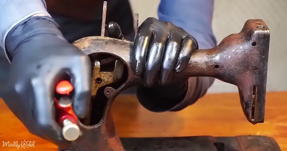 A gloved hand holds a rusted, mechanical part with a red tool inserted.