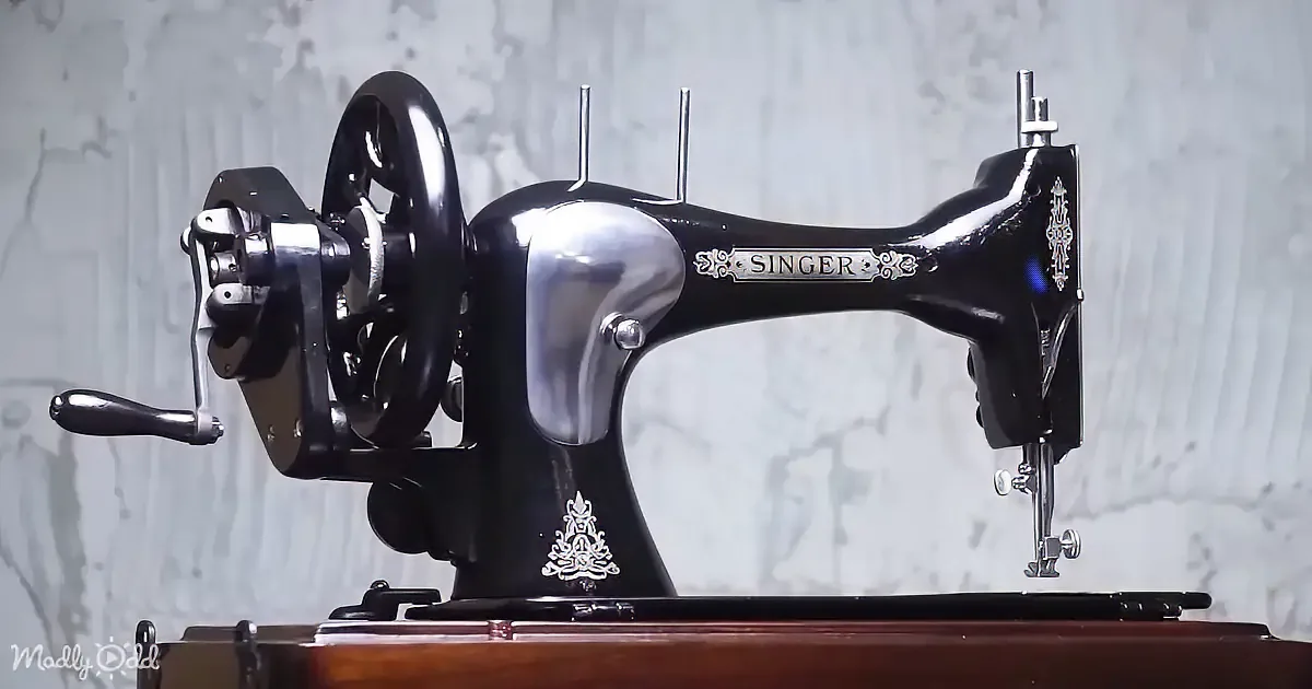 A vintage Singer sewing machine with a wooden base and ornate silver detailing is displayed against a textured gray...