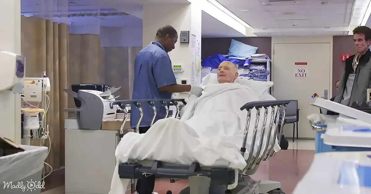 An elderly patient is lying in a hospital bed, covered with a white sheet, while a medical professional attends to them.