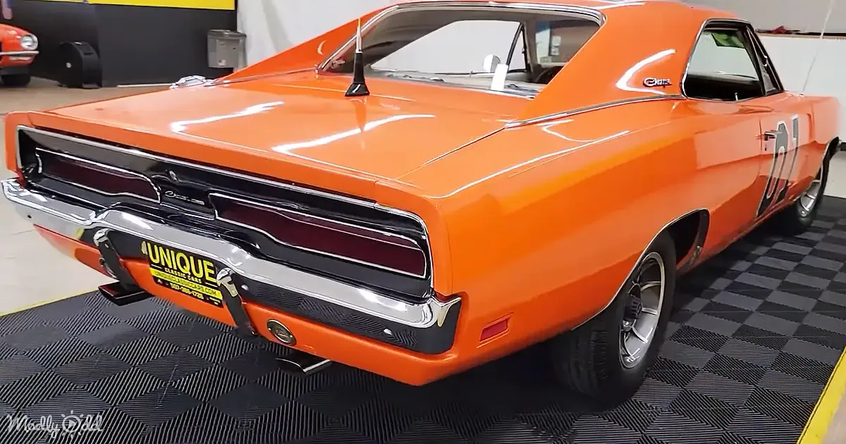 A bright orange classic muscle car with "The General Lee" number 66 on the side is displayed in a showroom.