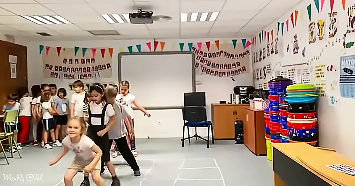 Children play hopscotch in a classroom decorated with colorful banners and educational posters.