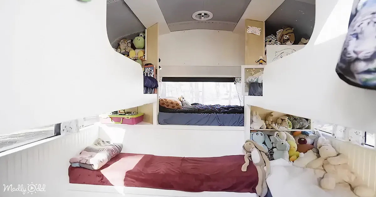 A cozy, compact bedroom with bunk beds, shelves filled with toys, and a window letting in natural light.