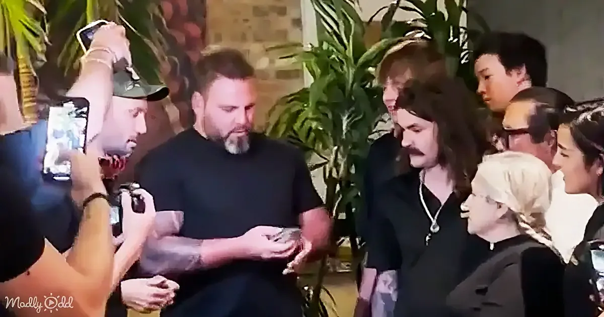 A man in a black shirt is surrounded by a group of people taking photos and videos.
