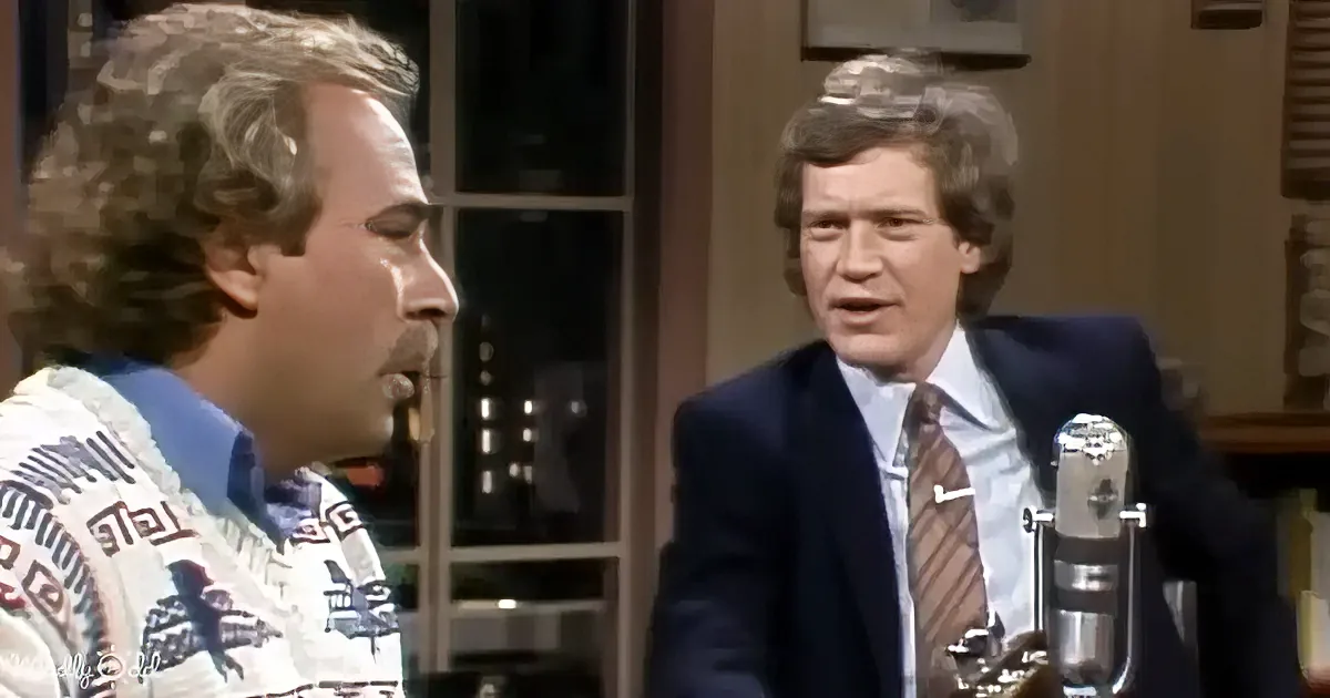 A man in a sweater is speaking to another man in a suit at a microphone.