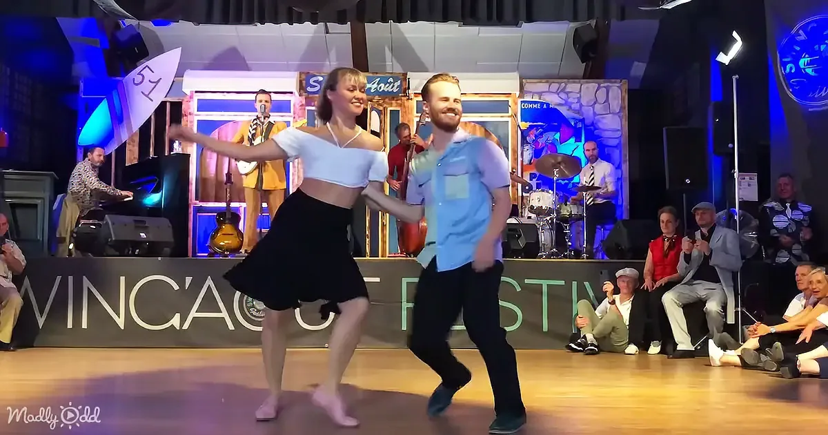 A couple dances on stage at the Swing'Ag Fest, with a band and audience in the background.