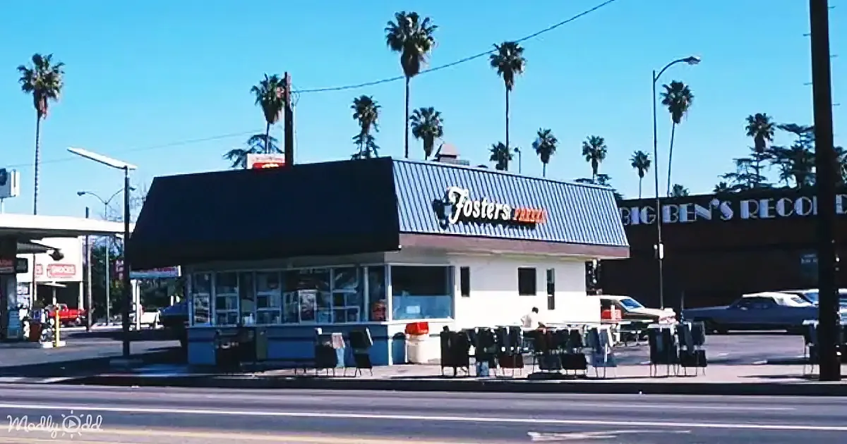 Fosters Pizza restaurant with palm trees, clear sky, and parked cars in the background.