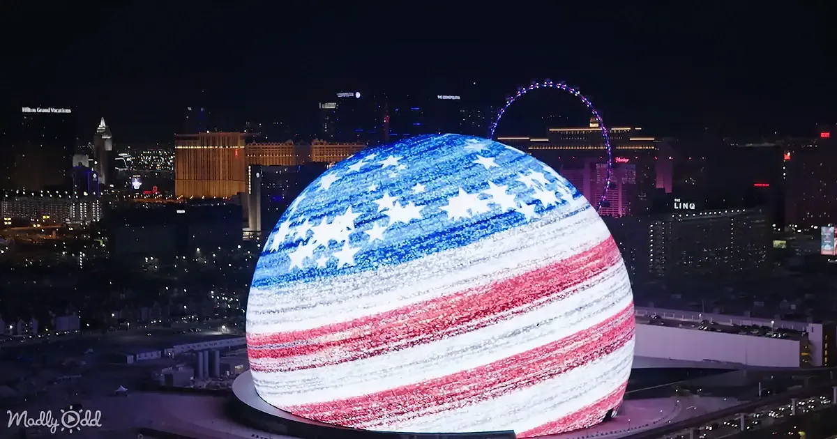 A large, illuminated sphere resembling the American flag dominates the foreground, with a cityscape featuring a Ferris...