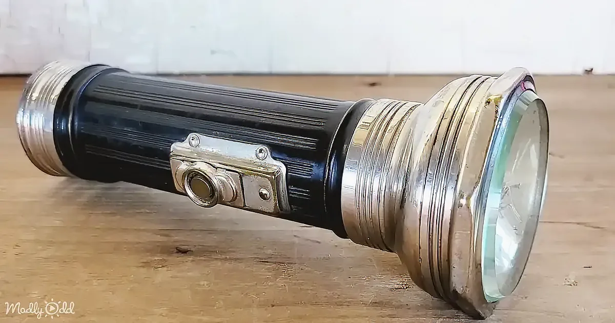 A vintage flashlight with a metallic finish and a central button is lying on a wooden surface.