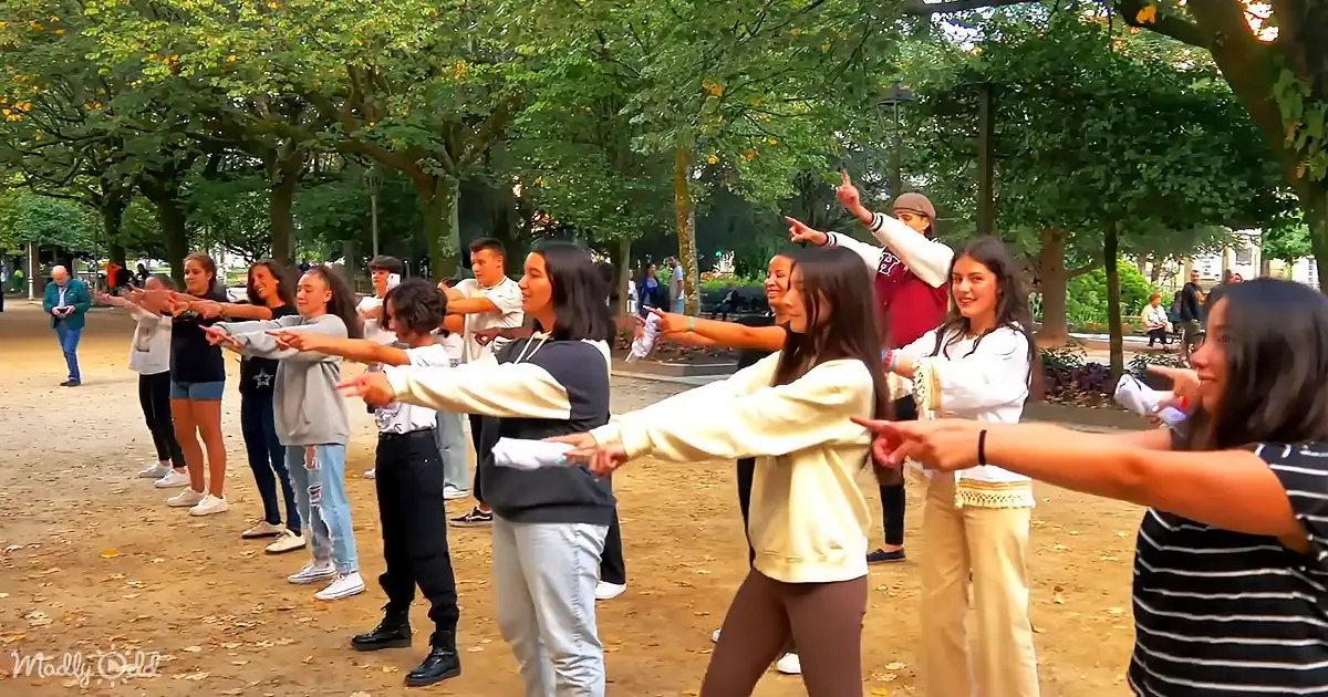 A group of people in a park are dancing in a line, pointing forward.