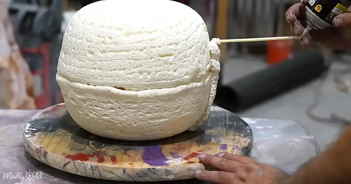 A person is applying white frosting to a large, multi-layered cake on a rotating stand.