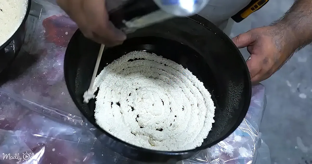 A person is mixing flour in a black bowl with a wooden spoon.