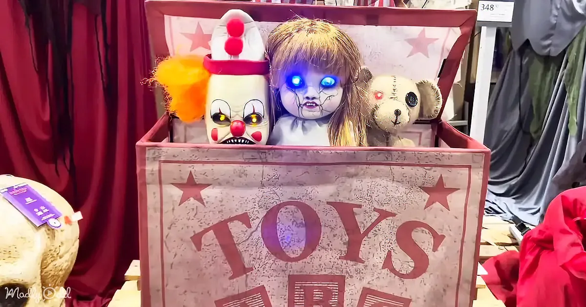 A creepy clown doll, a doll with glowing eyes, and a teddy bear sit in a box labeled "TOYS."