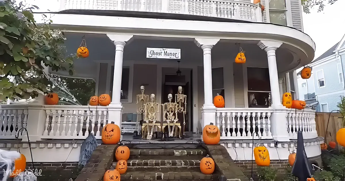 A spooky Halloween display with carved pumpkins, skeletons, and a "Ghost Manor" sign on a porch.