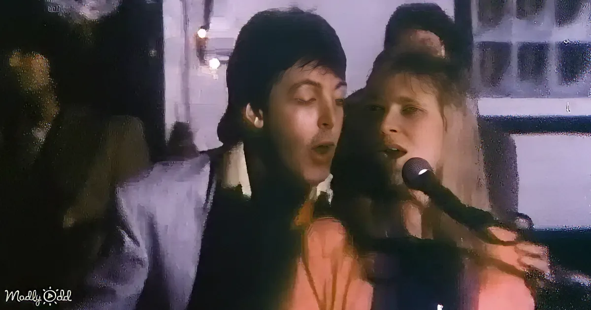 A man and woman sing into microphones, the man wearing a dark jacket and the woman in a light-colored top.