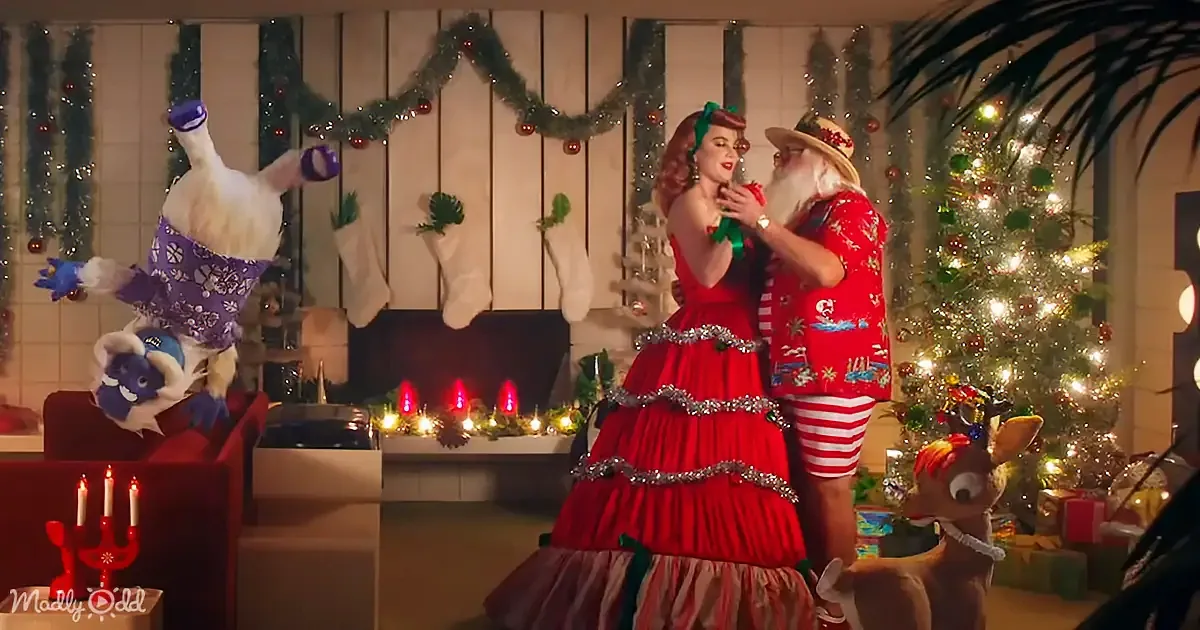 A festive scene with a woman in a red dress and Santa in a red shirt, surrounded by Christmas decorations and a reindeer.