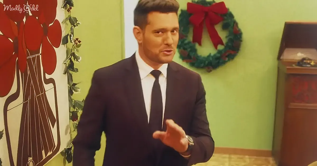 A man in a suit gestures while standing in a room with a Christmas wreath and floral artwork.