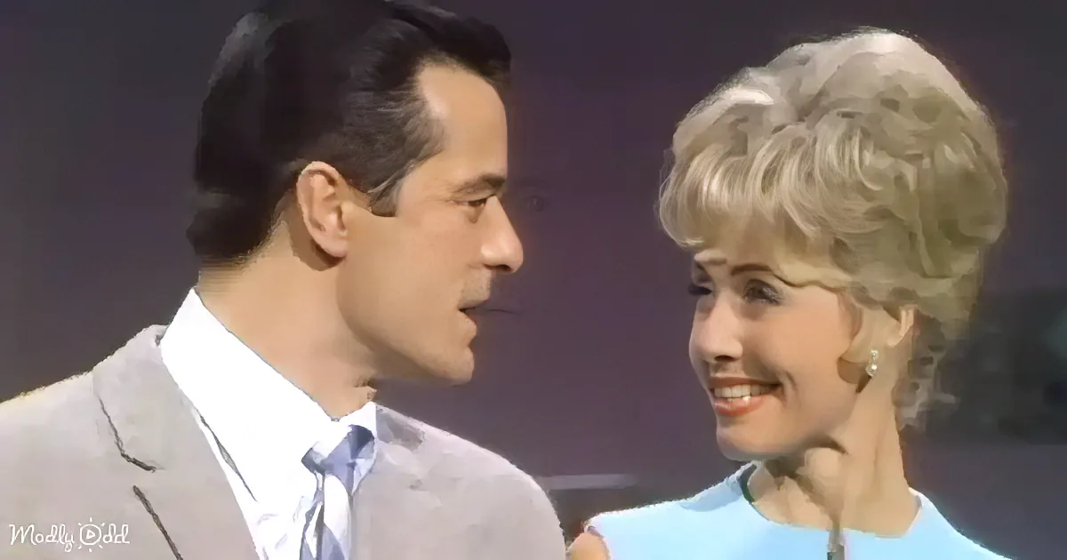 A man in a suit and tie stands beside a woman with blonde hair, both smiling.
