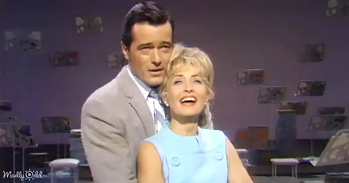 A man in a suit and a woman in a blue dress are smiling and standing close together.