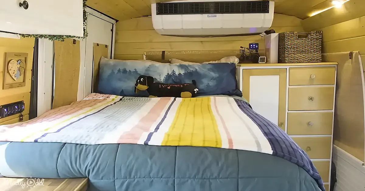 A cozy bed with colorful bedding and a dog pillow in a compact, well-lit room with wooden walls and a small dresser.