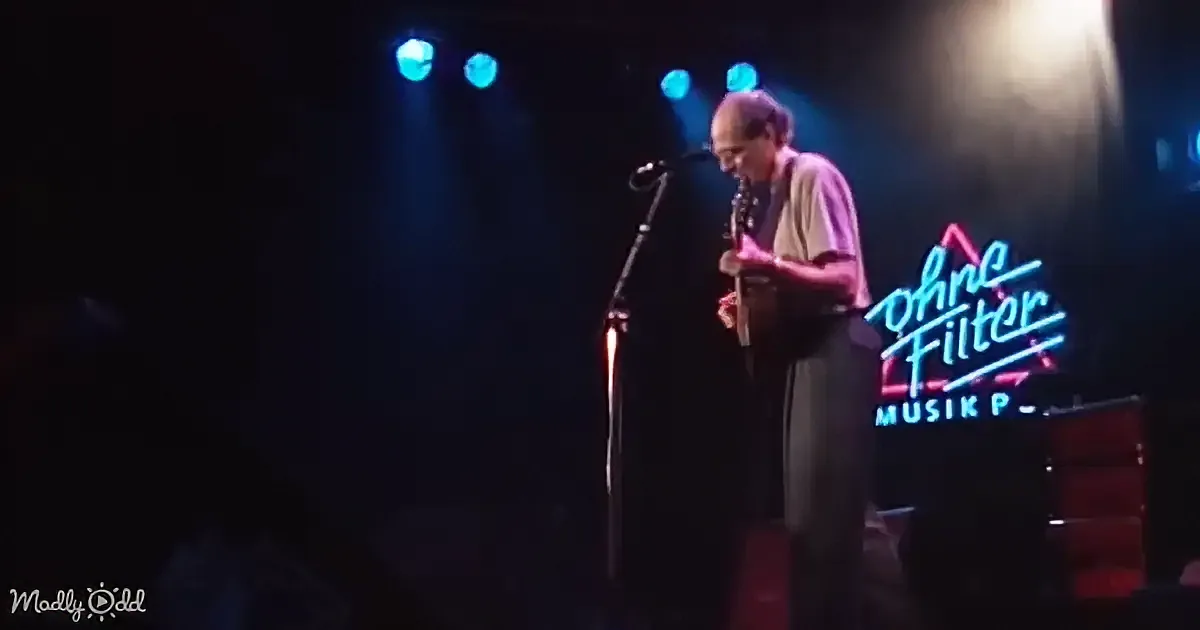 A man plays guitar on stage under blue lights, with a neon sign reading "Ohne Filter Musik" in the background.