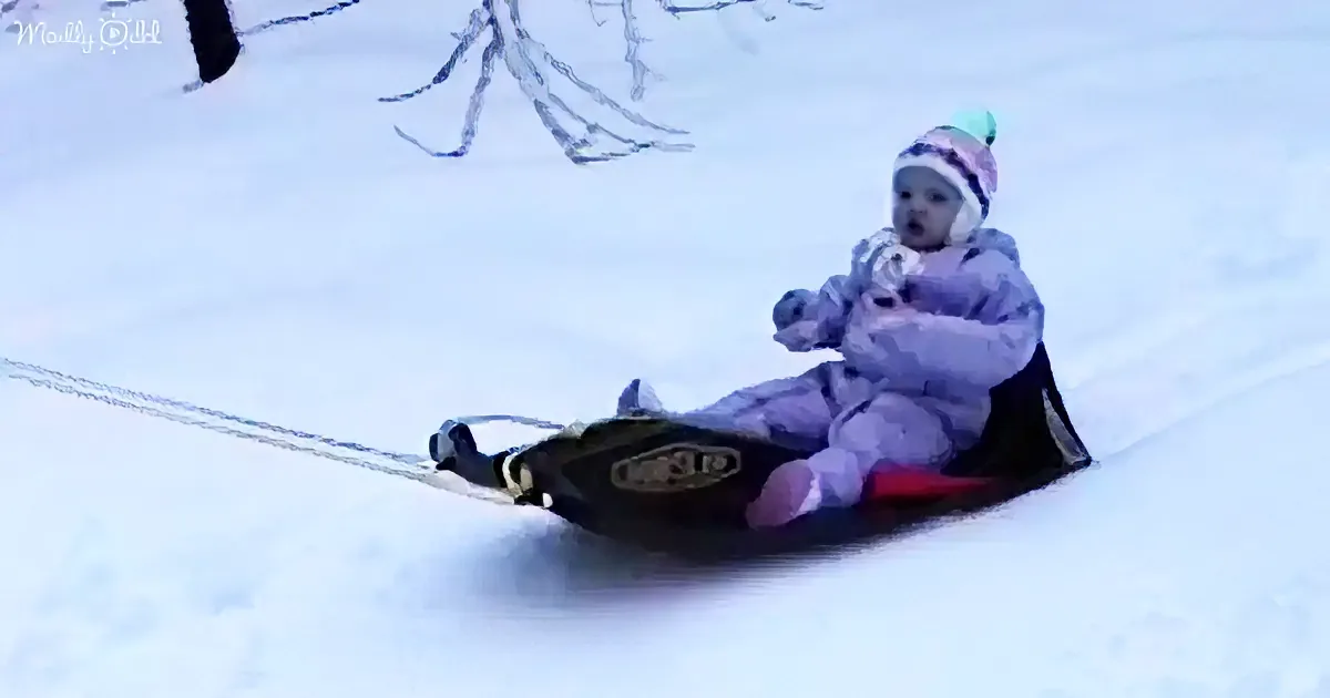 A child in winter gear sleds down a snowy hill, holding onto a rope.
