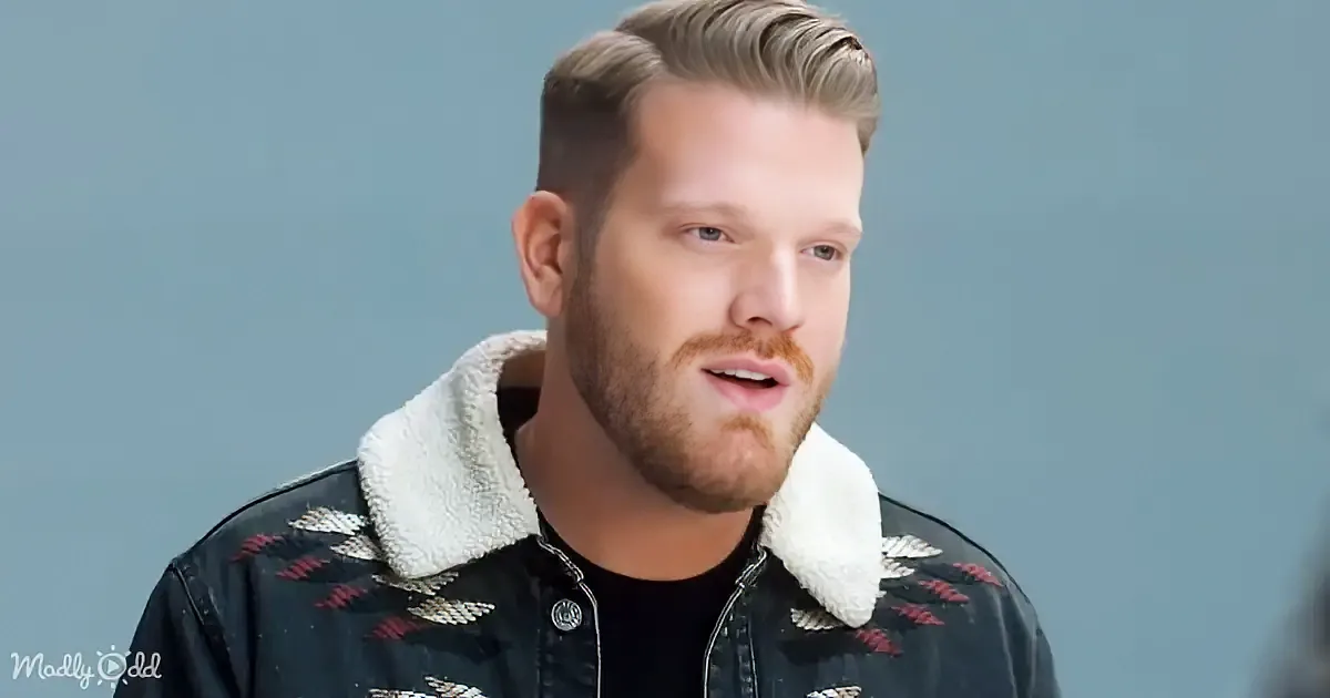 A man with a beard and short hair, wearing a black jacket with a white fur collar and a patterned design, is looking to...