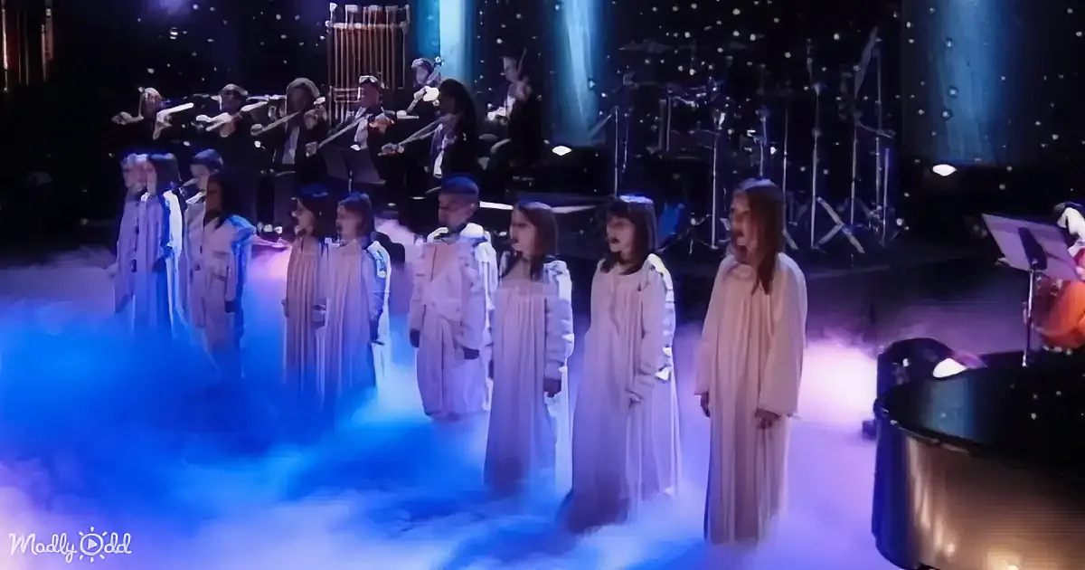 A choir in white robes sings on a stage with blue fog, accompanied by an orchestra.