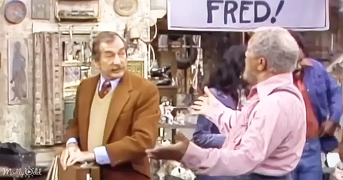 A man in a brown suit shakes hands with another man in a pink shirt in a cluttered shop.