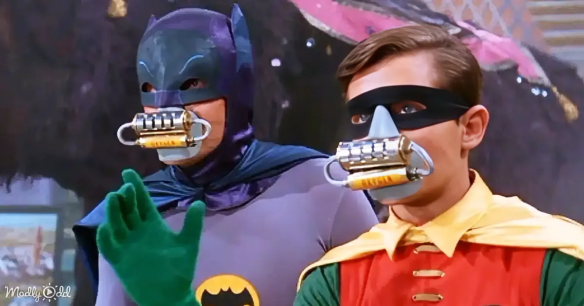 Batman and Robin, both with their mouths covered by devices, stand side by side.