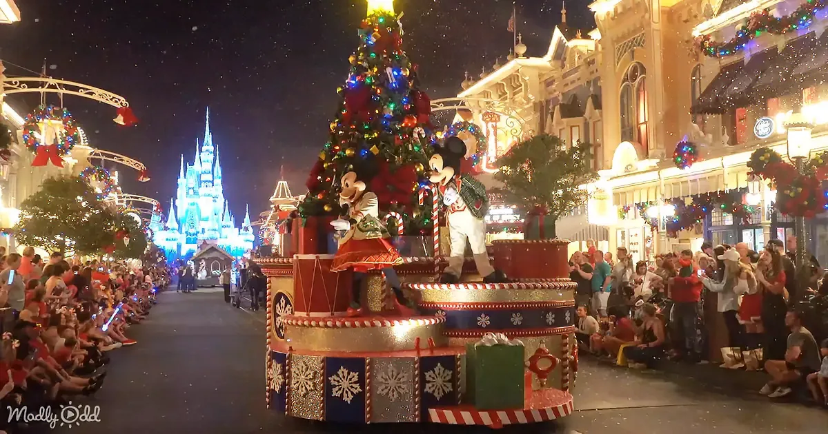 A festive Christmas parade float featuring Mickey Mouse and Minnie Mouse is being watched by a crowd under a starry night...