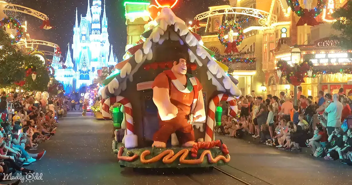 A large, animated gingerbread house float featuring a character in a red outfit is being paraded in a festive...