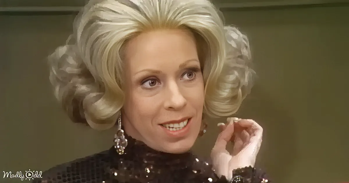A woman with voluminous blonde hair styled in large curls, wearing a black sequined top and large earrings, adjusts her...